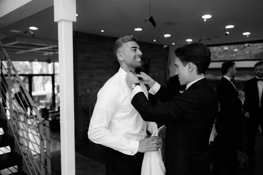 Groomsmen helping the groom with his tie before heading to the Bridgeport Art Center.