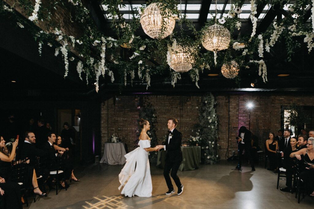 Bride and groom's first dance below elegant floral draped lighting during their reception at Revel Space.