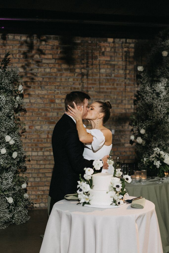 The bride and groom share a kiss in front of their wedding cake at the reception.