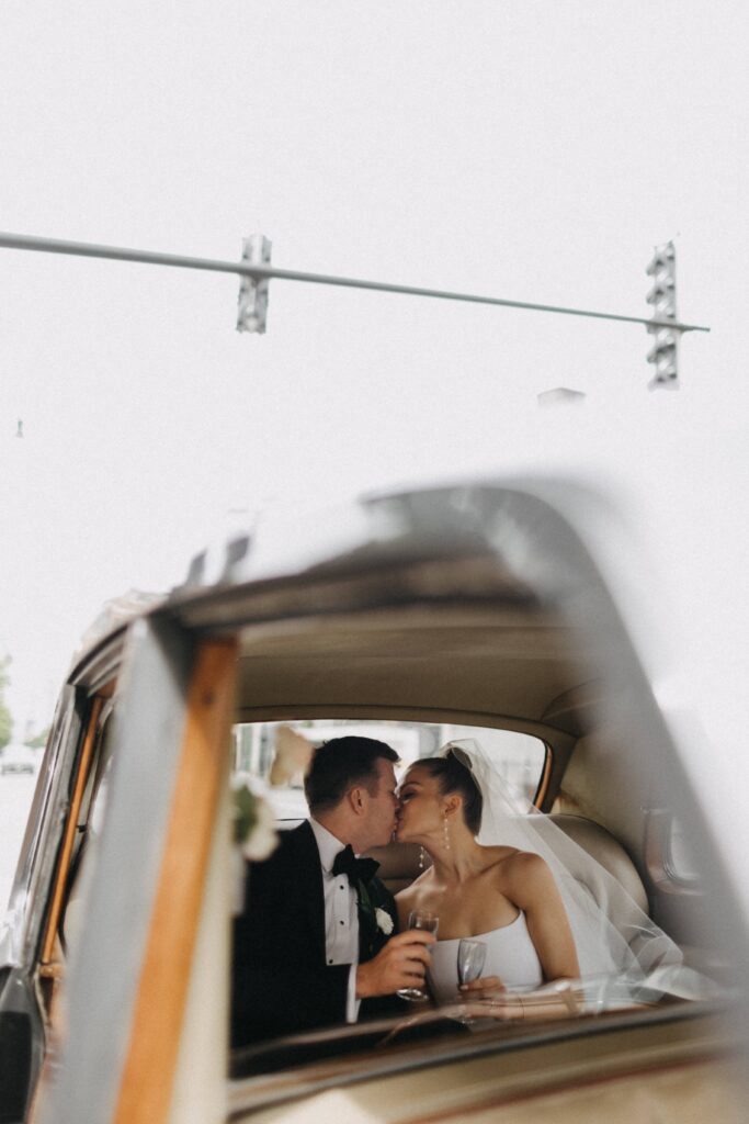 Bride and groom share a candid kiss in the back of a Rolls Royce parked outside Revel Space.