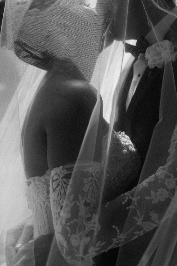 Bride and groom kiss in black and white shot under veil