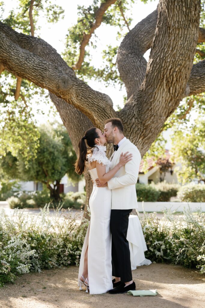 Bride and groom kiss in front of the Wishing Tree on the Artist Cottage Lawn at Ojai Valley Inn